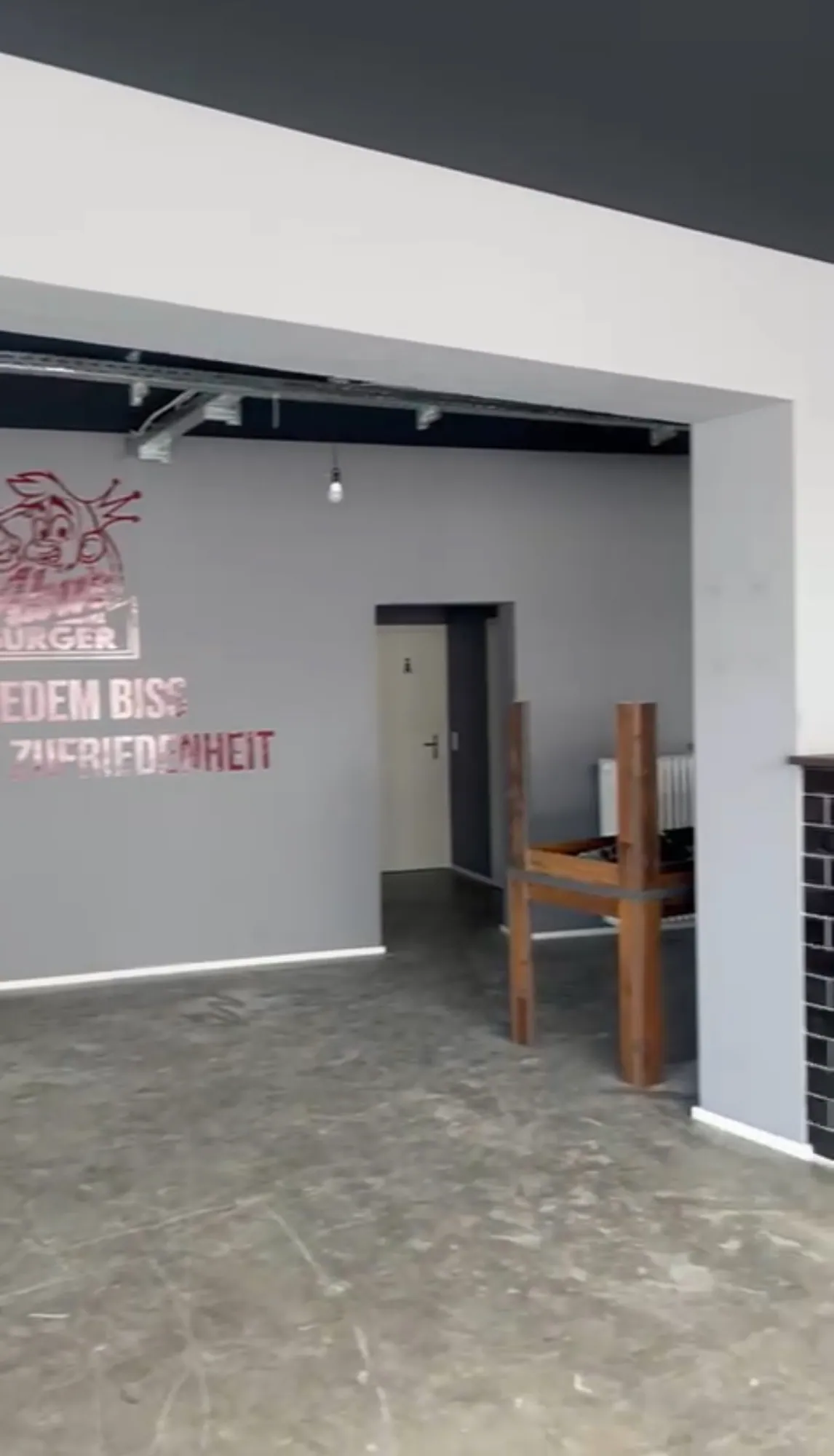 Leerer Gastraum von Abu’s Burger im Umbau mit grauem Estrich und rotem Logo-Schriftzug an der Wand